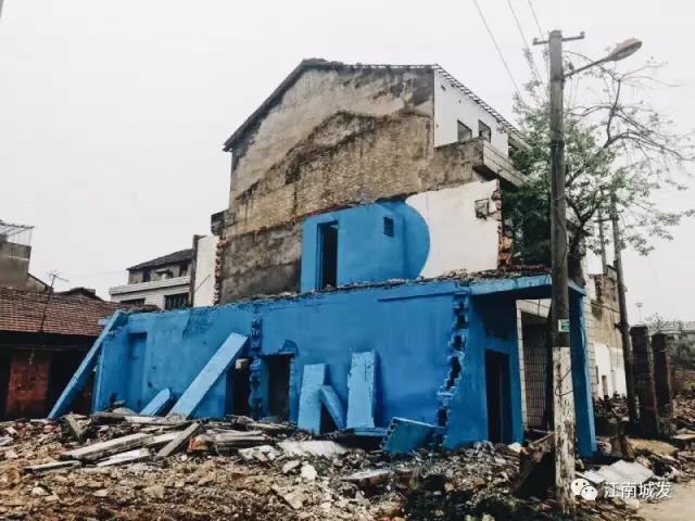 △ 這棟建筑是臨江最近的半拆遷建筑物的遺留，沅江和堤壩成為了展覽的天然背景。創(chuàng)作團隊對這棟建筑進行了半涂裝，將符號性的沅水曲線與拆遷進行中的建筑立面進行意義的疊造，它們共同觸發(fā)了場所空間多元語境的生成，把拆遷這種暫時破壞性、干擾性的介入行動與沅水右岸發(fā)展的未來性、美好性緊密融合。